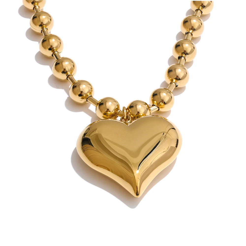 Gold heart-shaped pendant on a gold beaded necklace against a white background