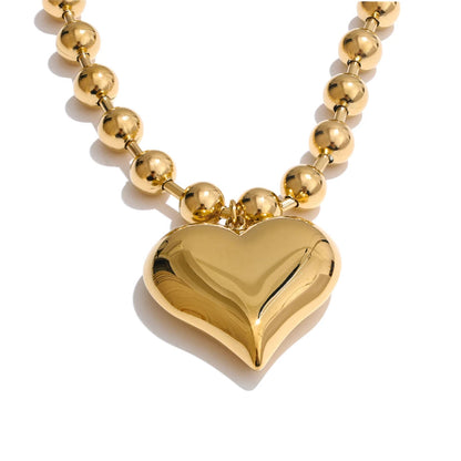 Gold heart-shaped pendant on a gold beaded necklace against a white background