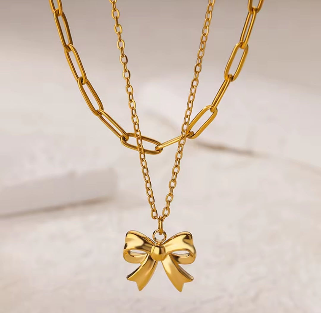 Gold chain necklace with a bow pendant on a light background