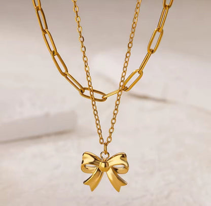 Gold chain necklace with a bow pendant on a light background